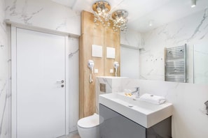 A modern bathroom with a marble wall, a wooden vanity, a white sink, and a shower area.