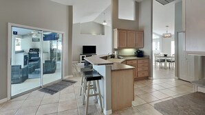 Een moderne keuken met een bar, schuiframen naar een terras en een eethoek met een kroonluchter.