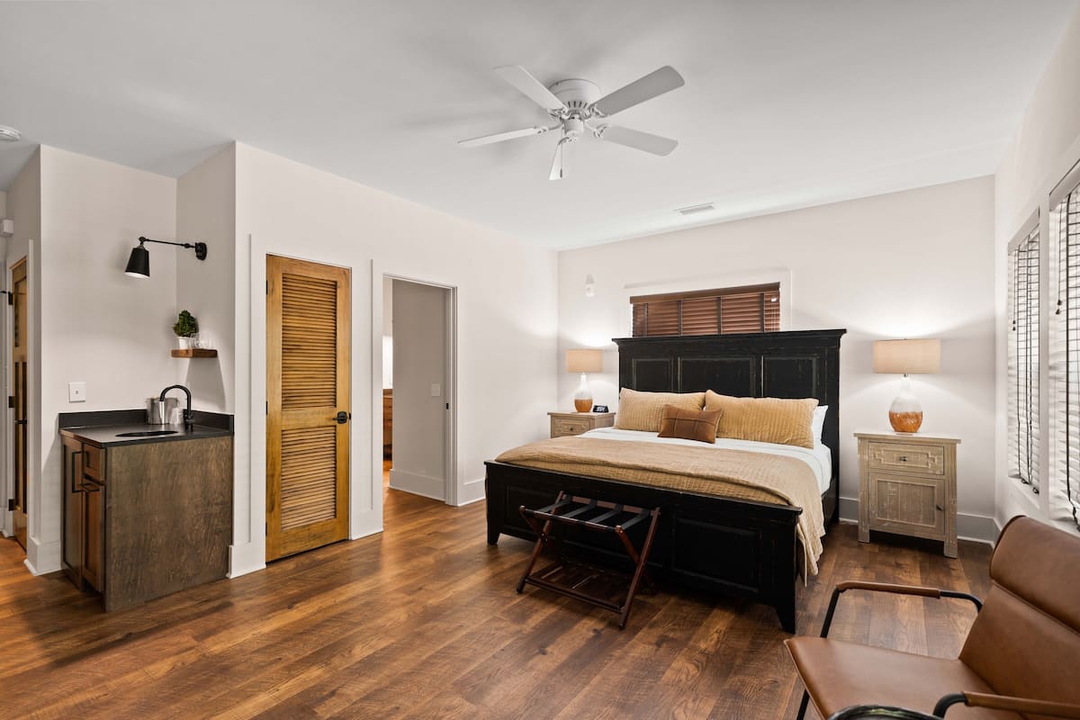 A bedroom with a bed, bedside tables, a ceiling fan, and a wooden door.
