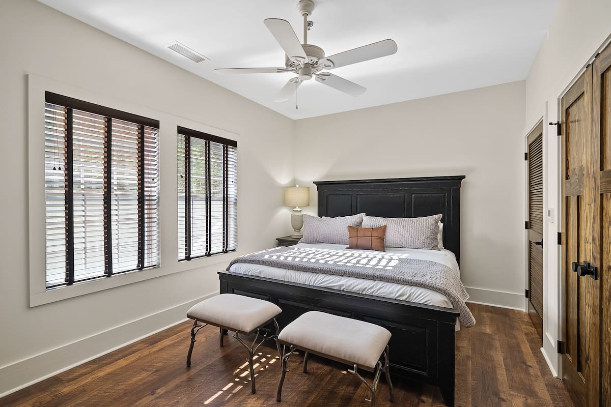 A bedroom with a large bed, two matching nightstands, a ceiling fan, and a window with blinds.