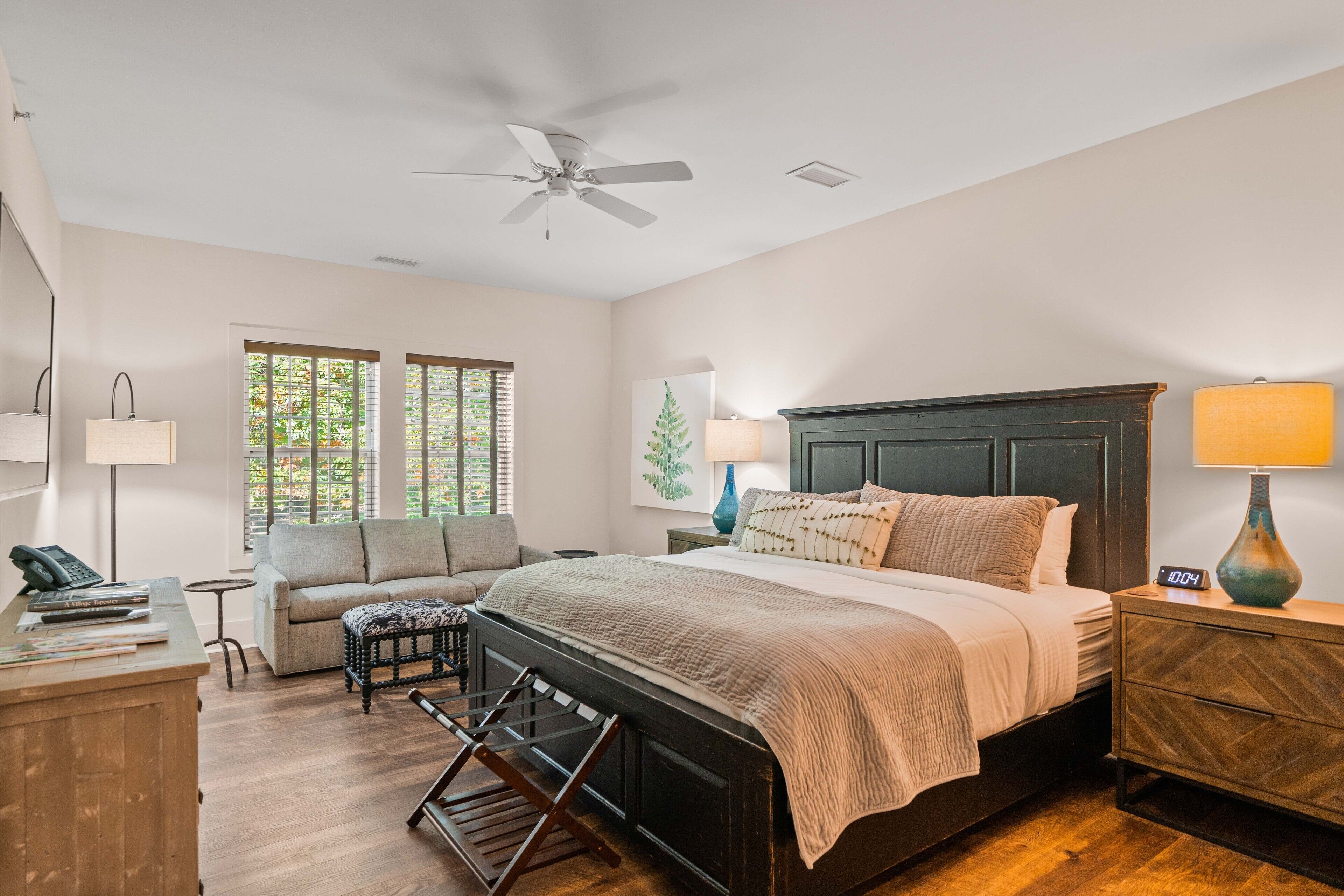 A bedroom with a bed, a desk, a chair, a sofa, a lamp, and a ceiling fan.