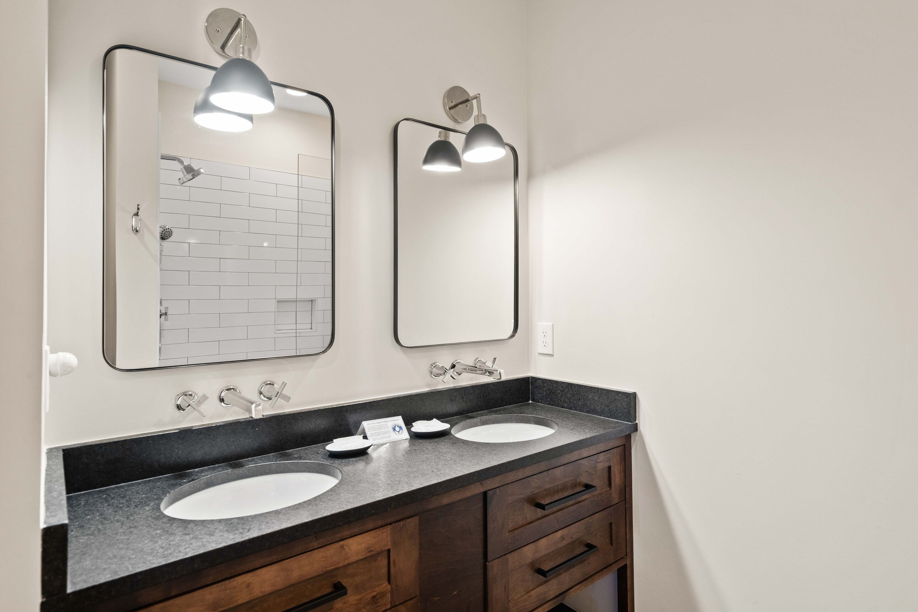 A bathroom with two sinks, a mirror, and a shower.
