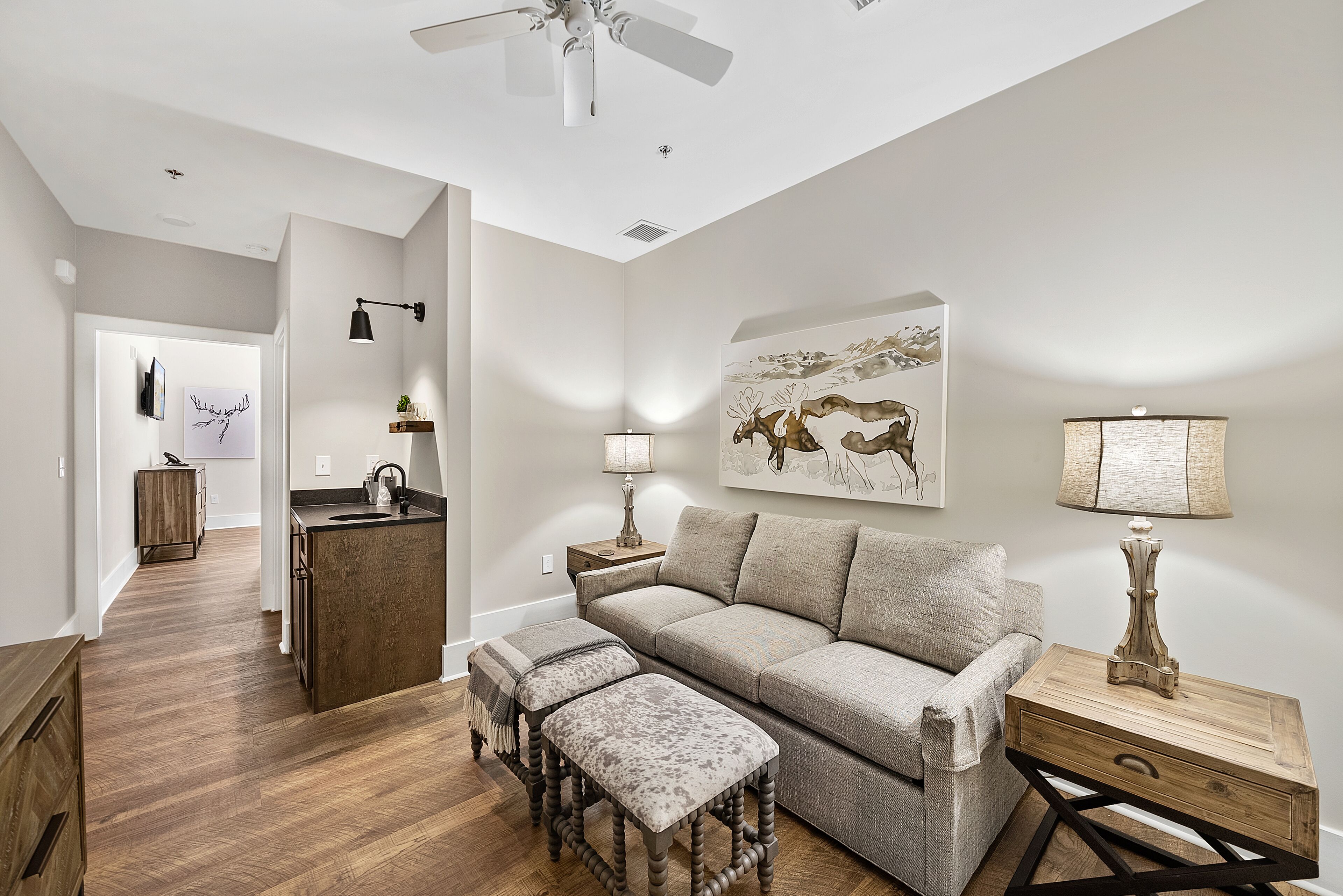 A modern living room with a sofa, ottoman, and side table, a ceiling fan, and a painting on the wall.