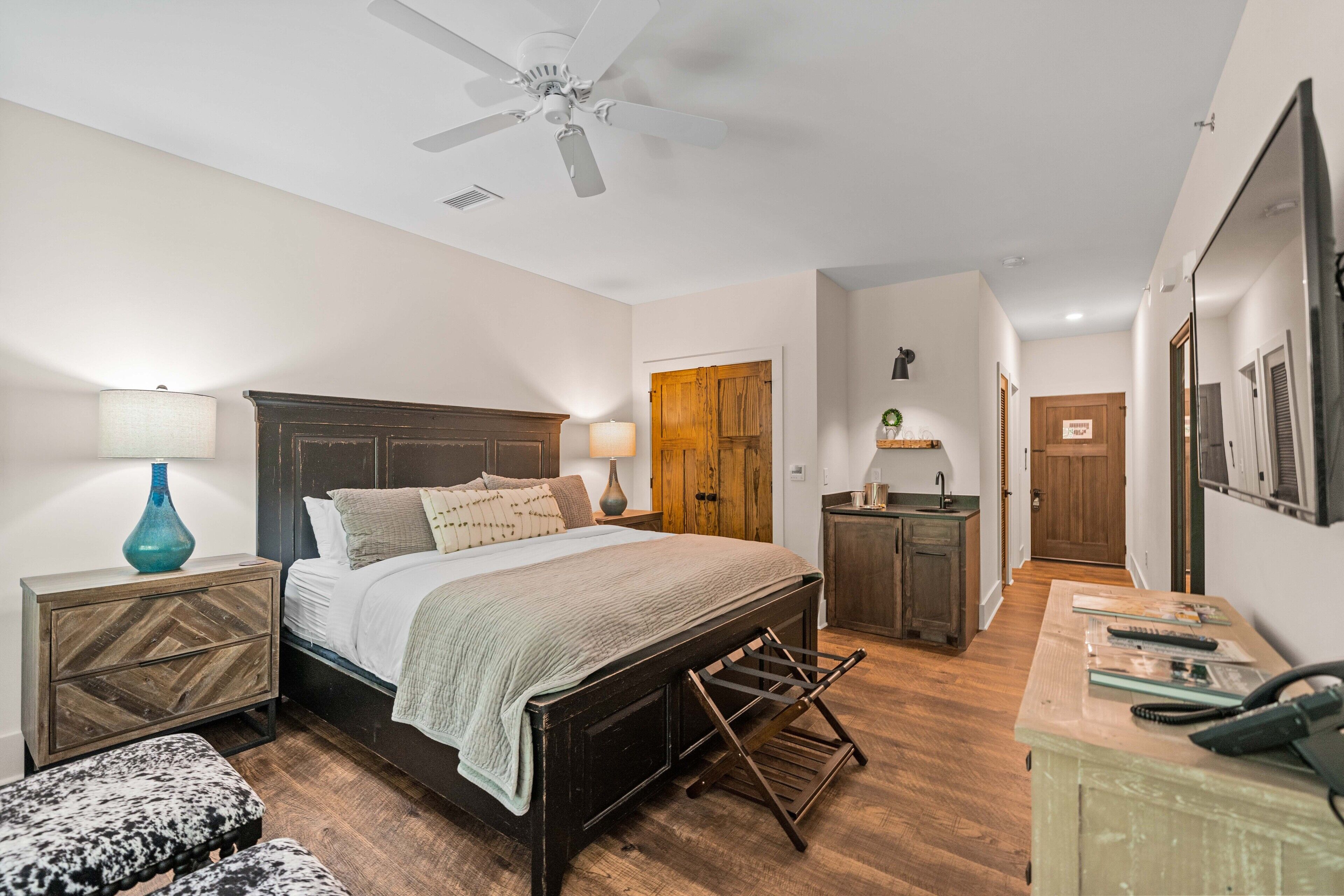 A bedroom with a bed, bedside tables, a nightstand, a bench, a desk, and a ceiling fan.