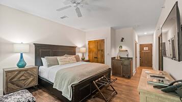 A bedroom with a bed, bedside tables, a nightstand, a bench, a desk, and a ceiling fan.