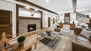 A spacious living room with a stone fireplace, wooden beams, a coffee table, and a leather sofa.
