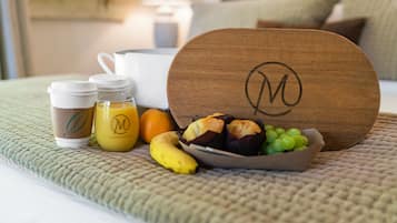 A breakfast setup with coffee cups, a banana, a bowl of fruit, and pastries on a bed.