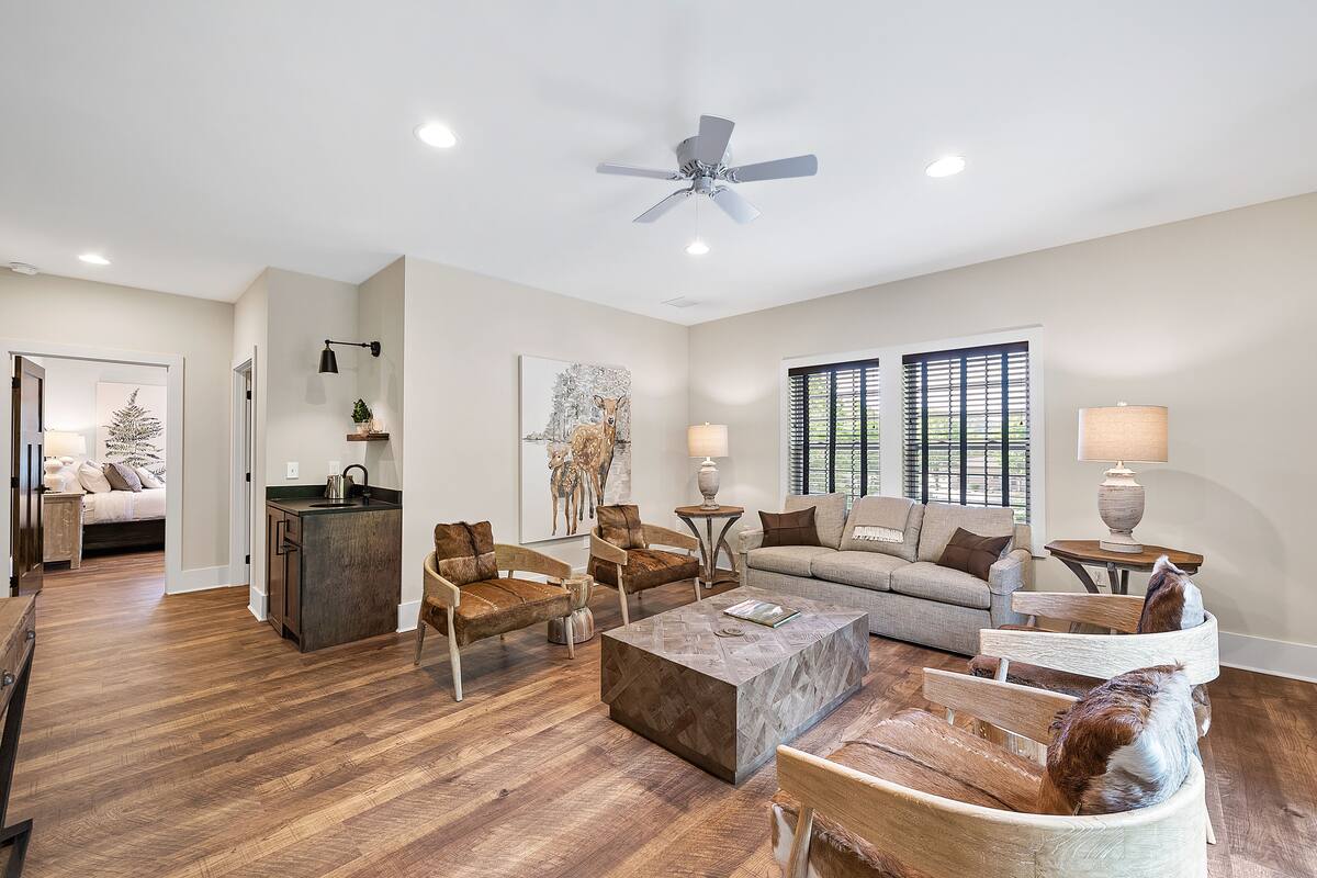 A spacious living room with a wooden floor, a ceiling fan, a sofa, a coffee table, and a dining area with a bench.