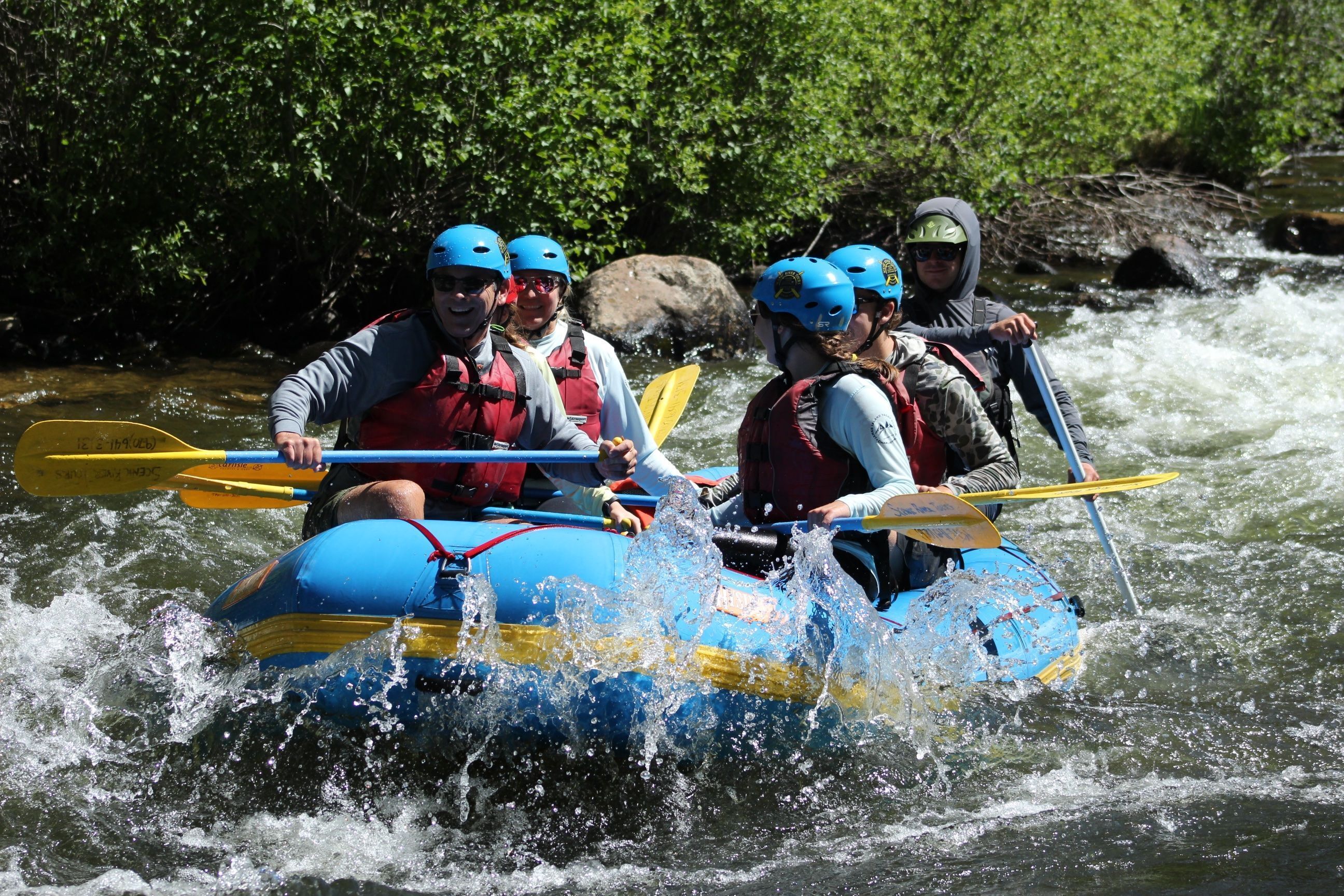 A group of people in a blue and yellow raft navigating a river.