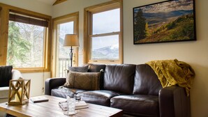 A cozy living room with a leather sofa, a wooden coffee table, and a large window with a view of the outdoors.