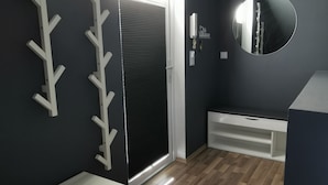 Une pièce moderne avec un mur foncé, un banc blanc, un miroir et une porte avec des stores.