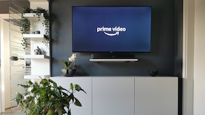 Un salon moderne avec un téléviseur à écran plat diffusant du contenu « Prime Video », un meuble de rangement blanc en dessous et une plante en pot au premier plan.