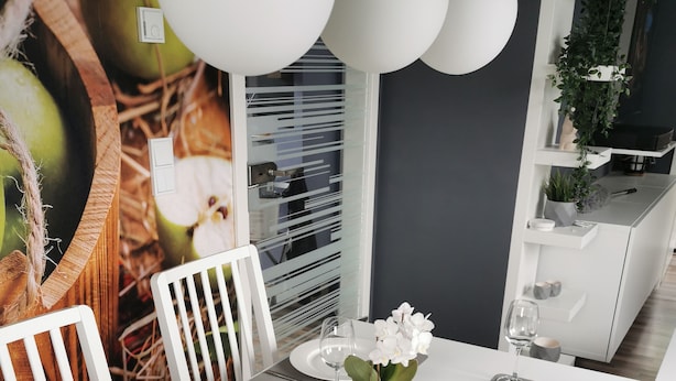 Une table à manger dressée avec de l’argenterie, des assiettes blanches et des verres à vin, entourée de chaises blanches.