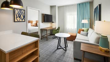A hotel room with a dining table, a sofa, a TV, and a desk.