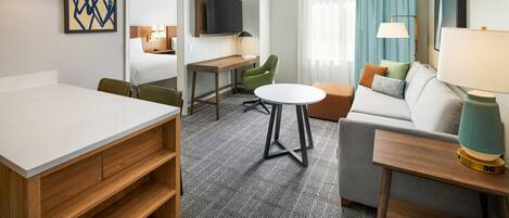 A hotel room with a dining table, a sofa, a TV, and a desk.