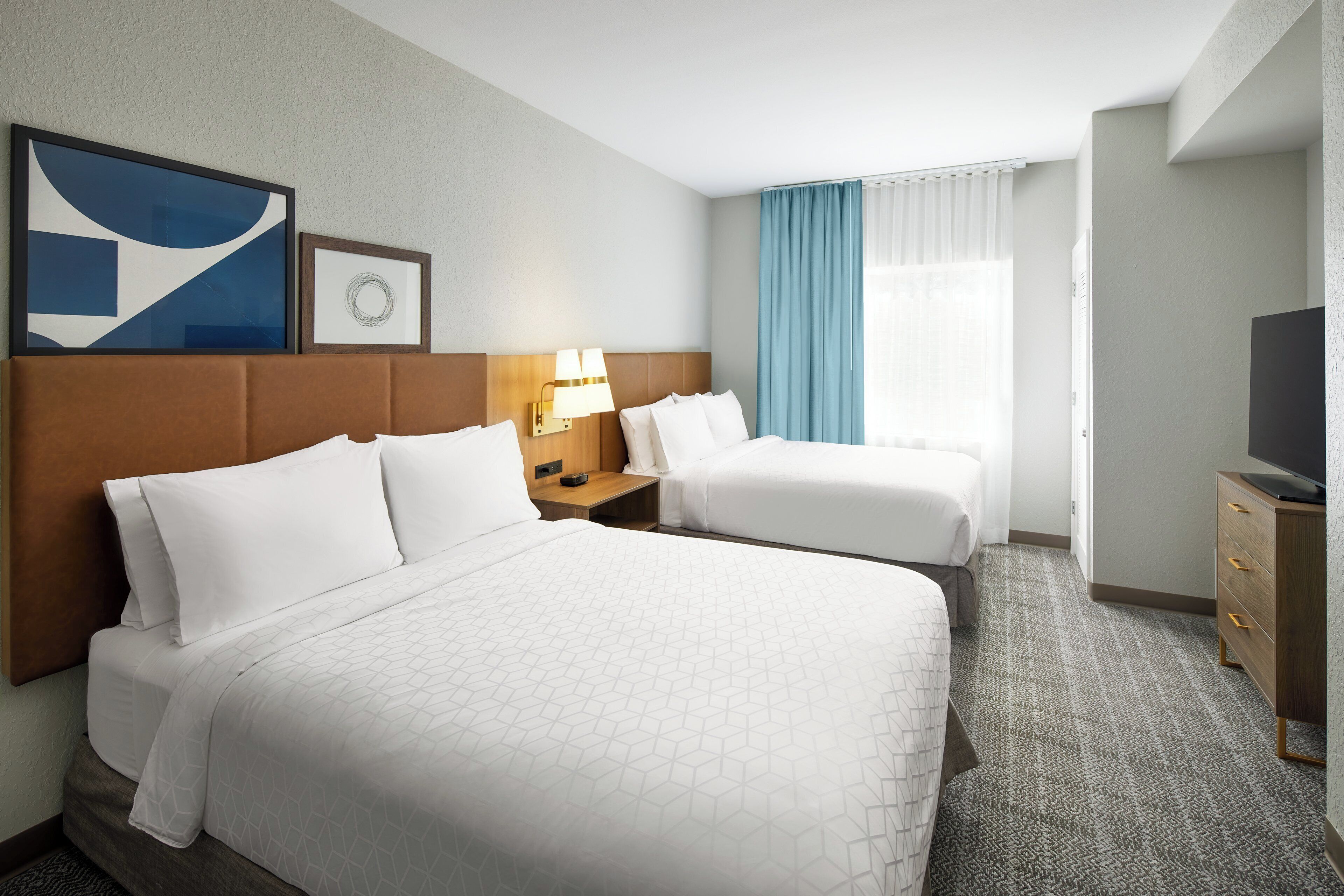 Een hotelkamer met twee bedden, een televisie, een bureau en een groot raam met gordijnen.