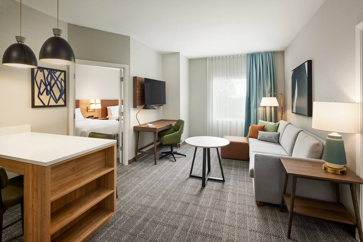 Ein Hotelzimmer mit Bett, Schreibtisch, Sofa, Esstisch und Fernseher.