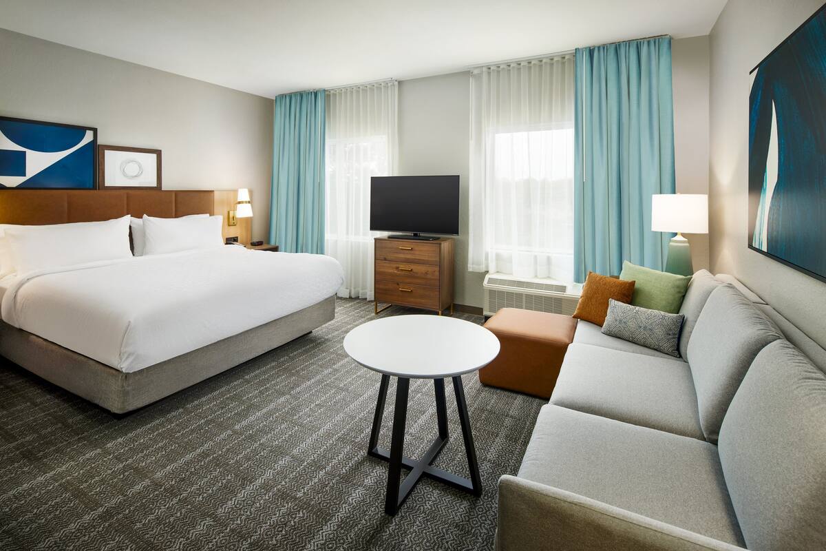 Ein Hotelzimmer mit einem Bett, einem Sofa, einem kleinen runden Tisch, einem Fernseher und einem Schminktisch.