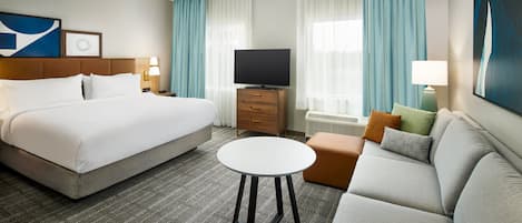 Ett hotellrum med en säng, en soffa, ett litet runt bord, en tv och en byrå.