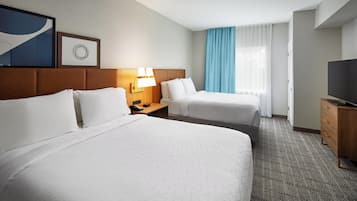 Habitación de hotel con dos camas, un escritorio, un televisor y una ventana con cortinas.