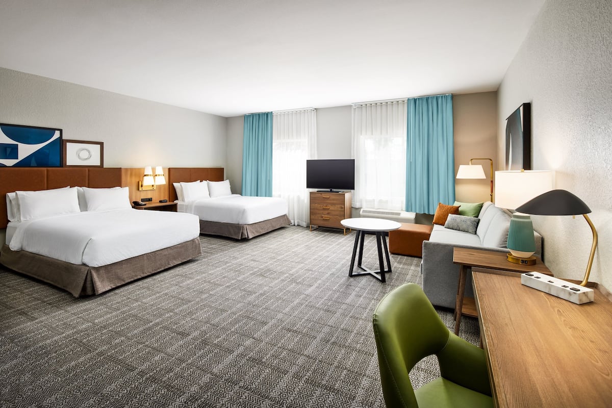 Ein Hotelzimmer mit zwei Betten, einem Fernseher, einem Schreibtisch und einem Sessel.