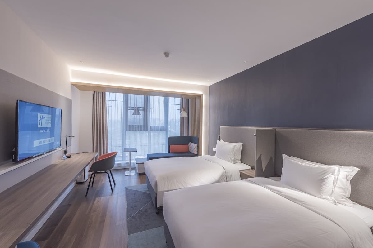 Una habitación de hotel moderna con dos camas, un televisor, un escritorio y un ventanal grande.