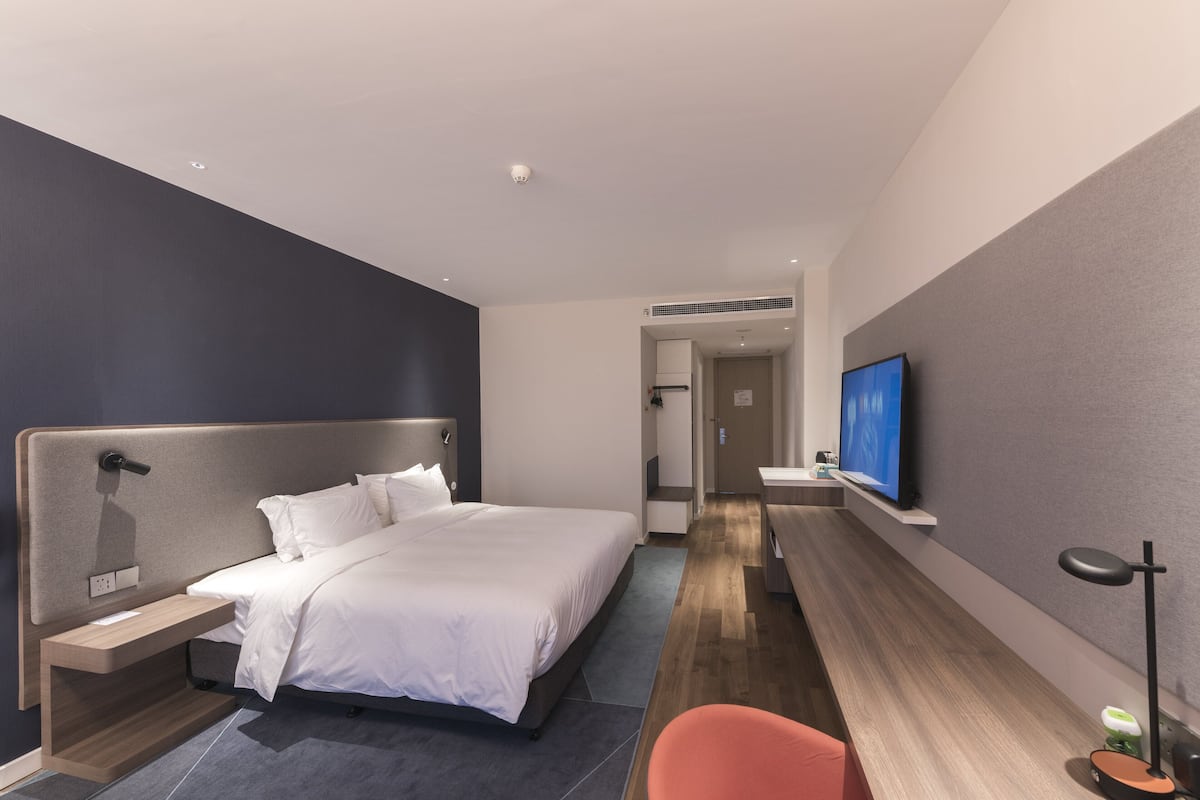 Una habitación de hotel moderna con una cama grande, un escritorio con televisor de pantalla plana y una zona de estar con una silla.
