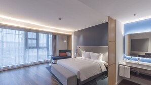 Une chambre d’hôtel moderne dotée d’un grand lit, d’un coin salon, d’une salle de bain avec un miroir et de grandes fenêtres offrant une vue sur la ville.