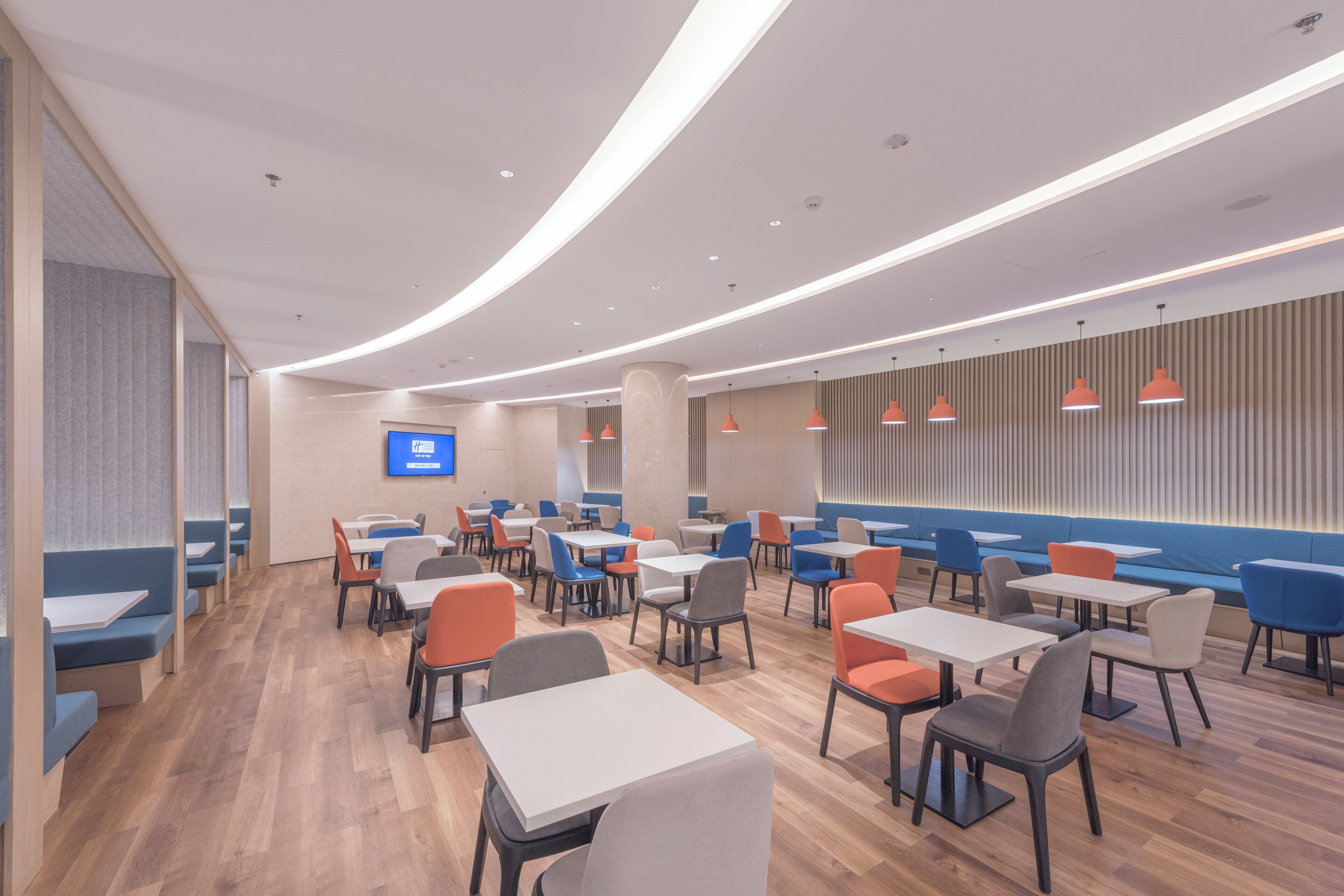 A modern restaurant with a variety of seating options including booths and tables, a flat-screen TV mounted on the wall, and pendant lighting.