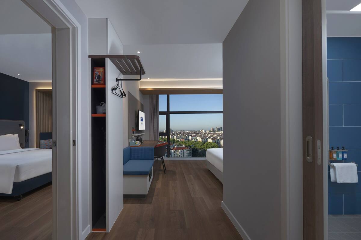 A modern hotel room with a large bed, a desk, and a view of the city.