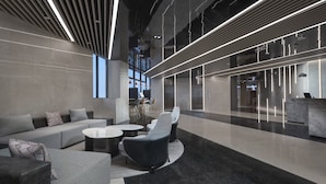 A modern lobby with a seating area, a reception desk, and a staircase leading to an elevator.