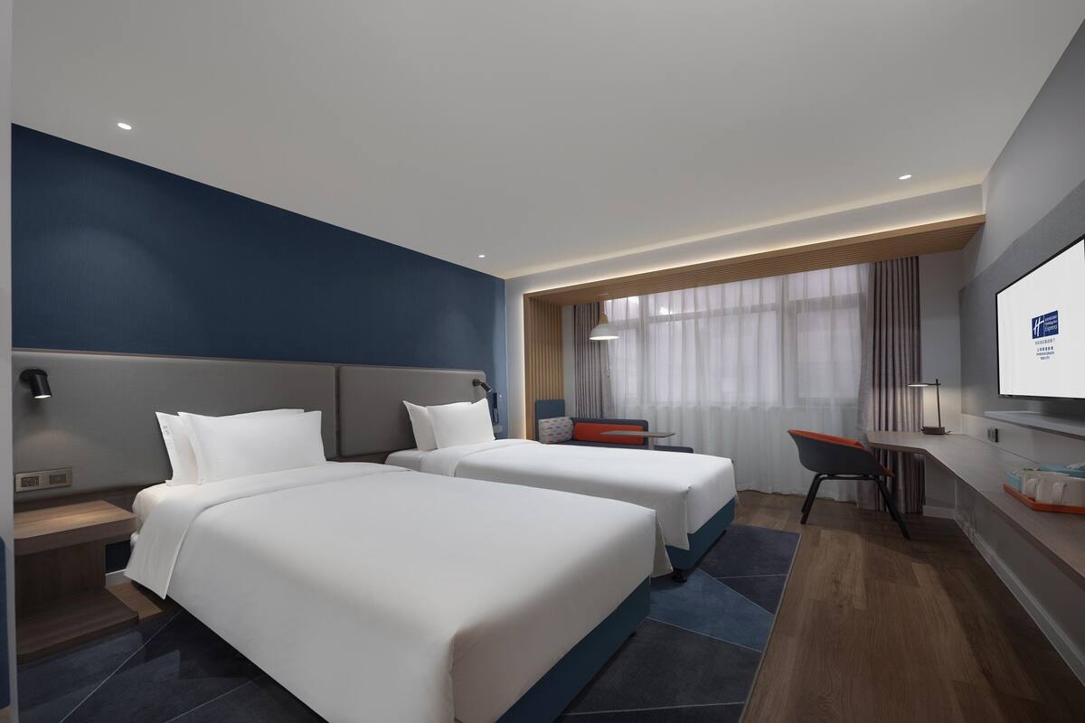 A modern hotel room with two beds, a desk, and a TV.