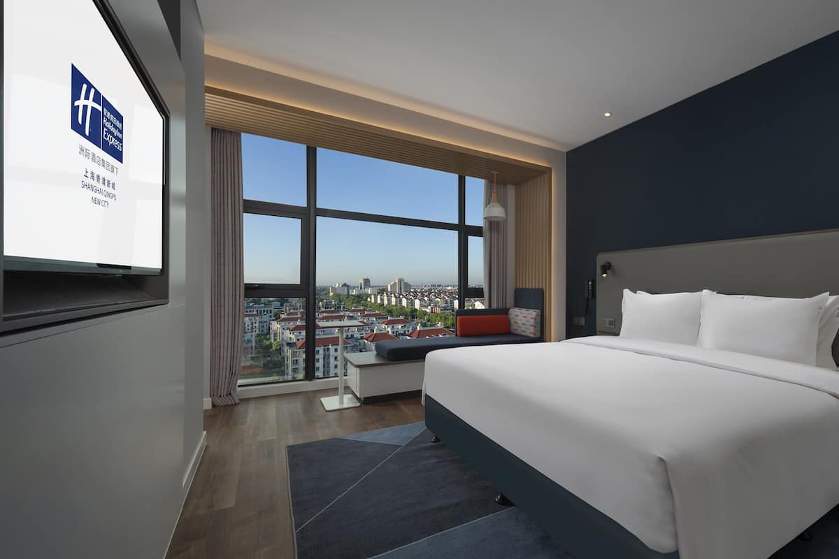 A modern hotel room with a large bed, a desk, and a view of the city.