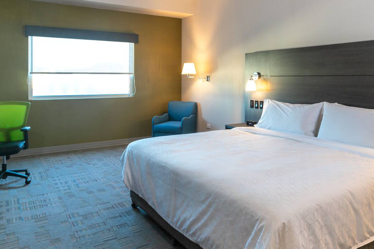 A hotel room with a large bed, a chair, a desk, and a window.
