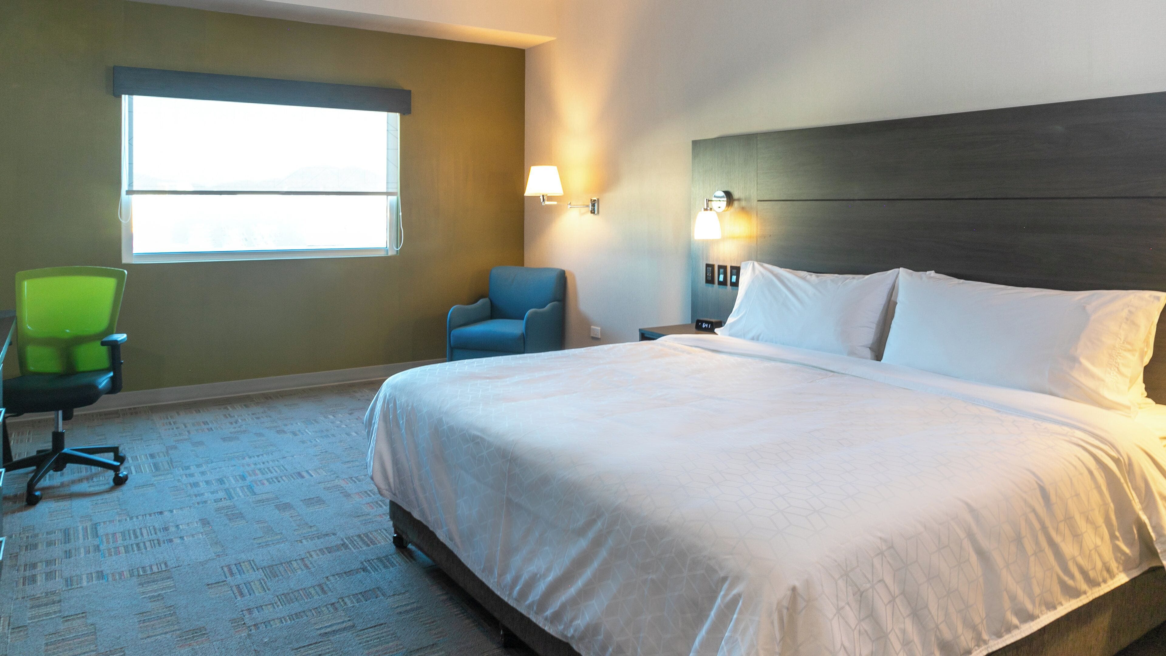 A hotel room with a large bed, a chair, a desk, and a window.