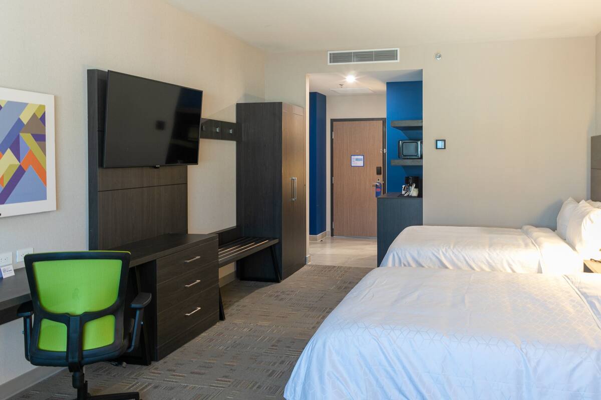 A hotel room with a bed, a desk with a chair, a television, and a door leading to another room.