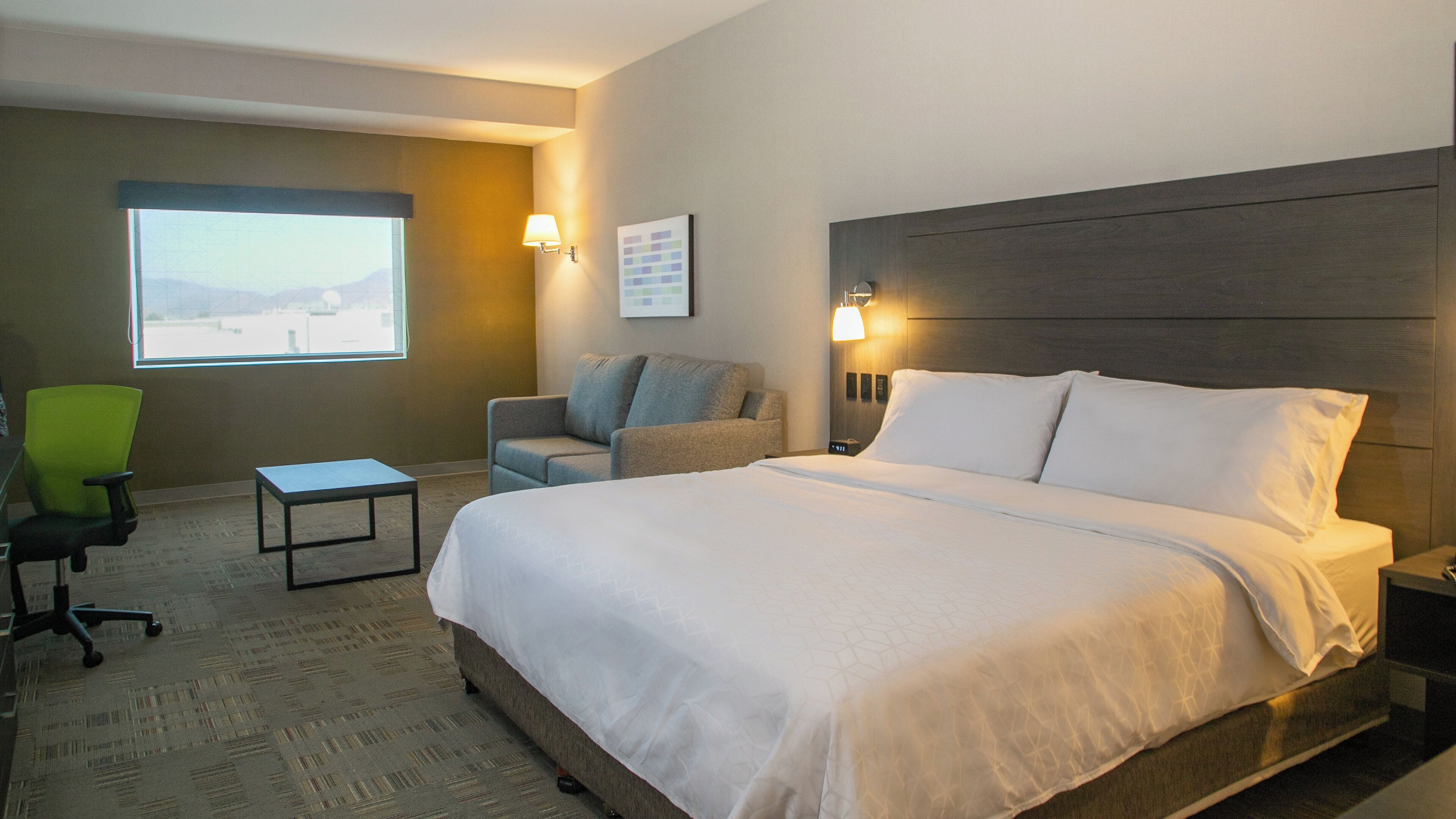 Une chambre d’hôtel avec un grand lit, un bureau, une chaise et une fenêtre donnant sur un beau paysage.