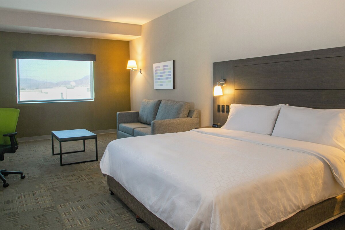 A hotel room with a large bed, a desk, a chair, and a window with a view.