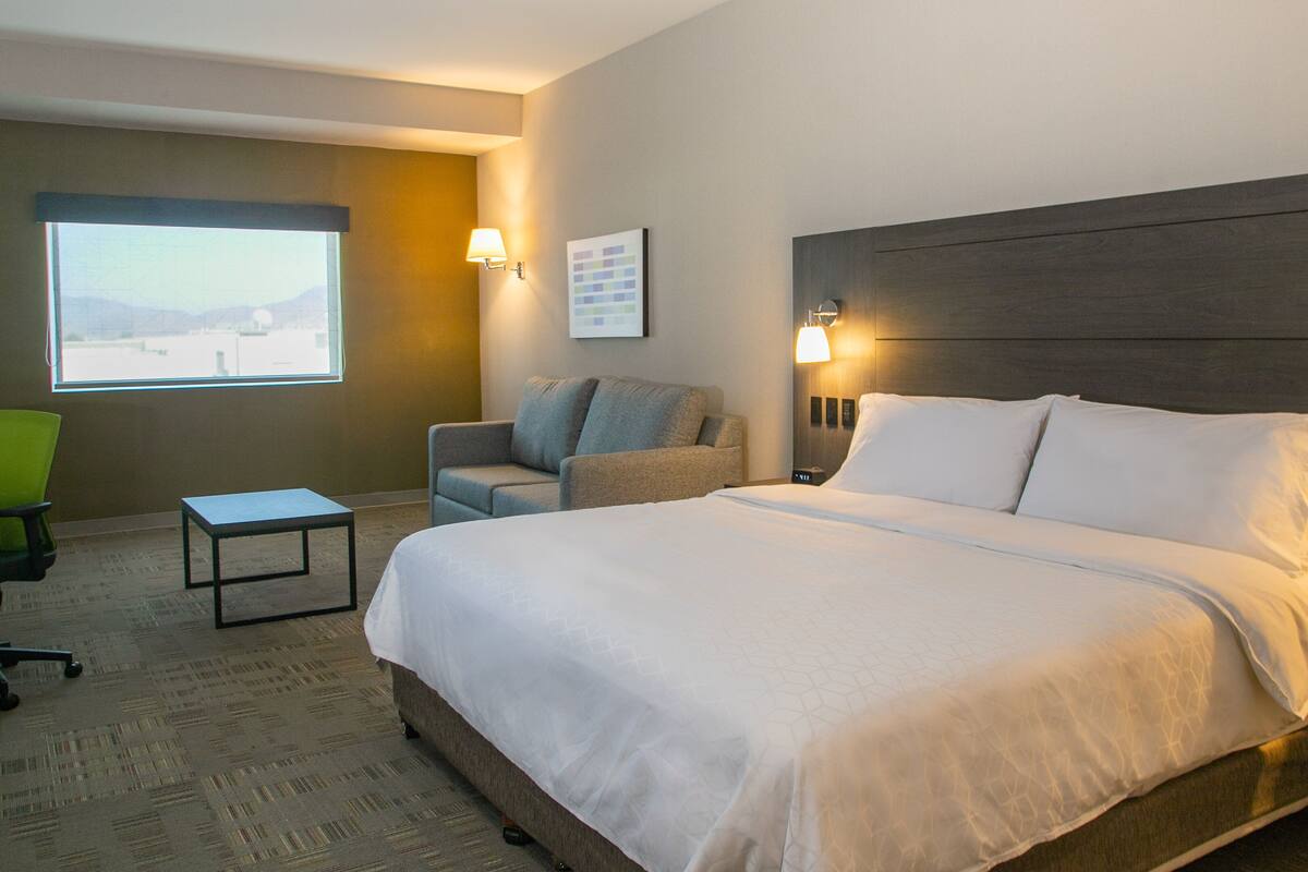 A hotel room with a large bed, a desk, a chair, and a window with a view.