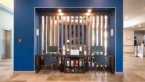 Un comptoir d’accueil équipé de deux écrans, d’une imprimante et de deux chaises, situé dans un hall d’entrée moderne aux murs bleus et au sol carrelé.
