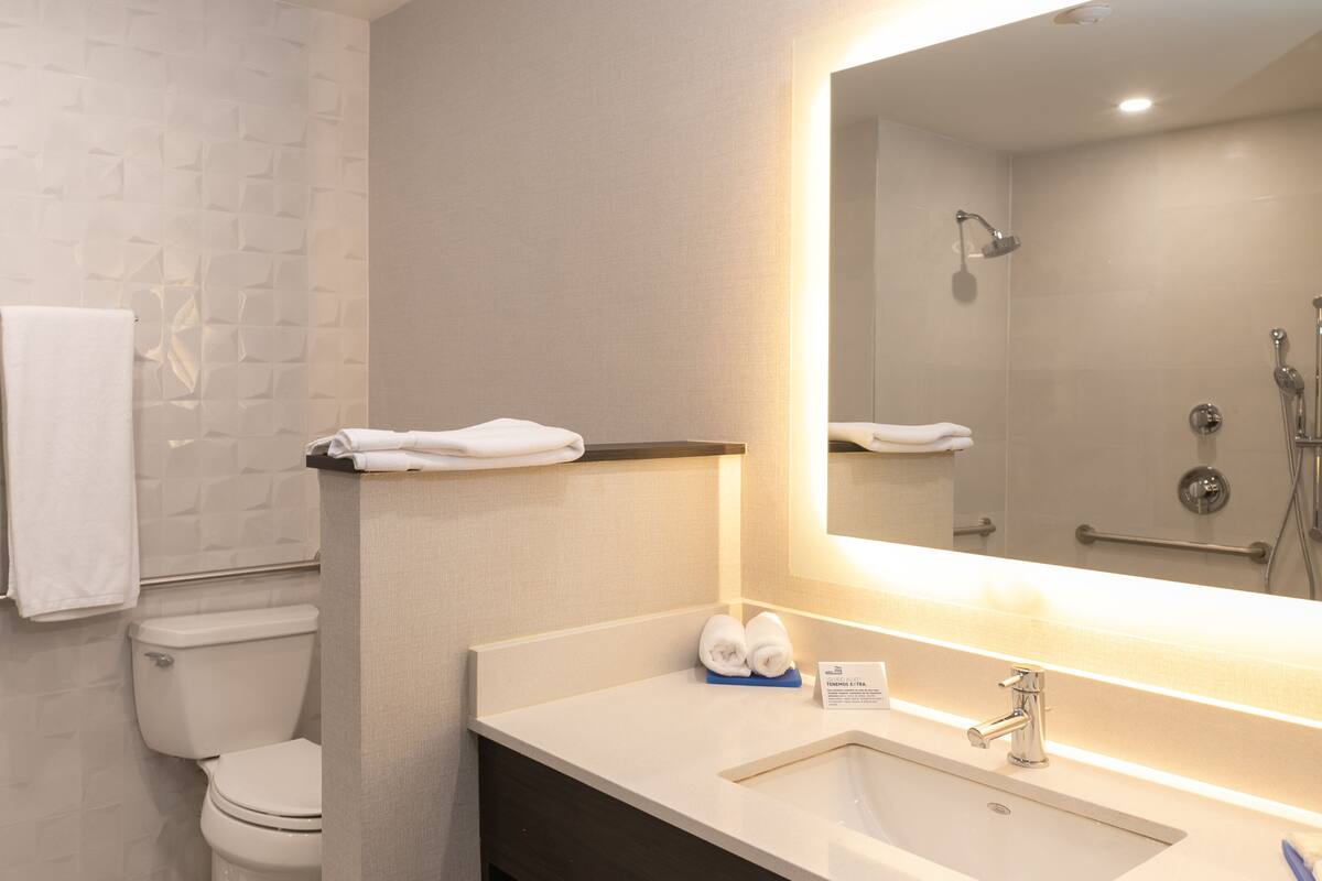 A modern bathroom with a white toilet, a sink with a mirror, and two towels hanging on the wall.