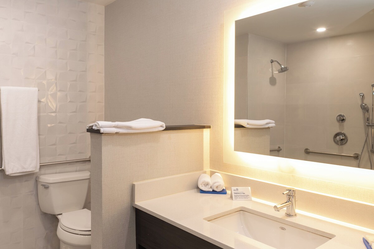 A modern bathroom with a white toilet, a sink with a mirror, and two towels hanging on the wall.