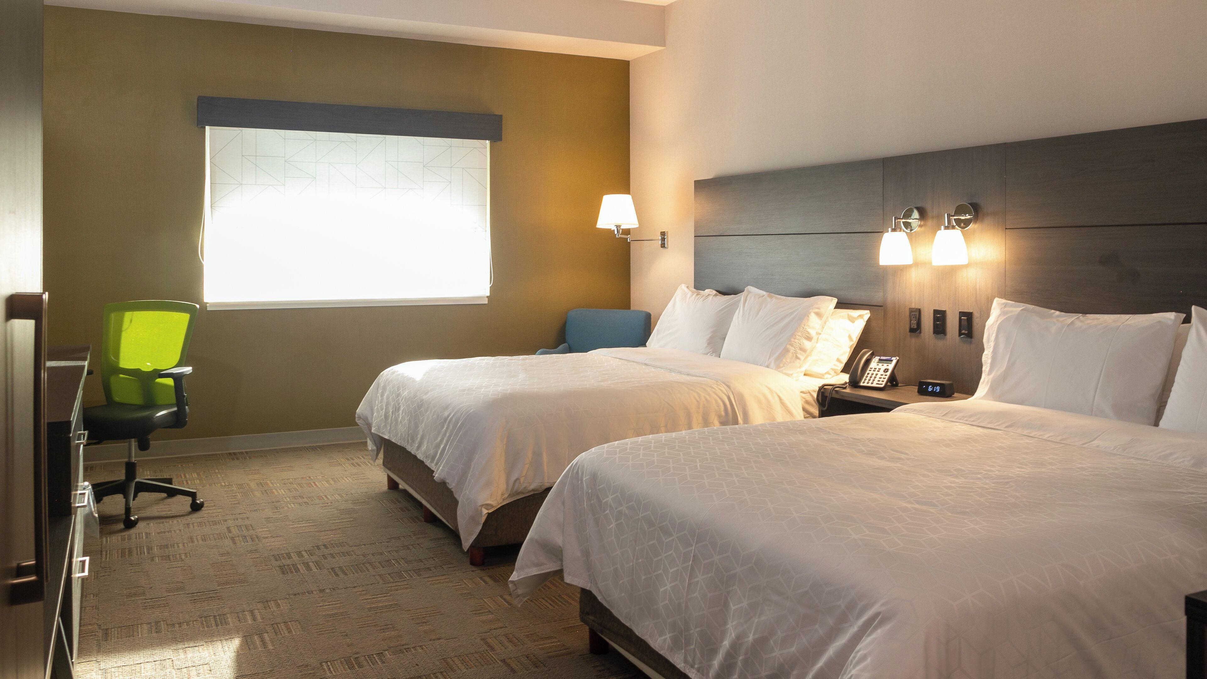 A hotel room with two beds, a desk, a chair, a window, and a wall-mounted phone.