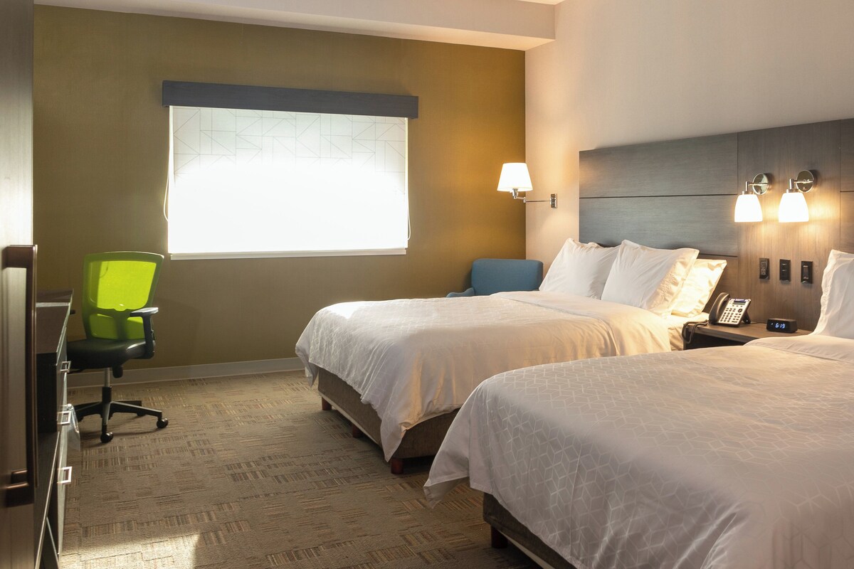 A hotel room with two beds, a desk, a chair, a window, and a wall-mounted phone.