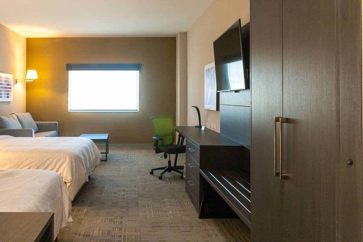 A hotel room with two beds, a desk, a chair, a TV, and a window.