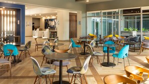 Un hall d’hôtel moderne doté de plusieurs espaces de détente, notamment des tables et des chaises rondes, et d’un comptoir de réception bien visible.