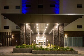 A hotel entrance with a modern design, featuring a stone facade, a covered entrance area, and a parking lot.