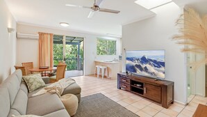 A living room with a sofa, TV, and a balcony with a view of mountains. - Baden 28 - Rainbow Shores. Top Floor Unit. Air conditioned. Walk to Beach (Rainbow Beach)