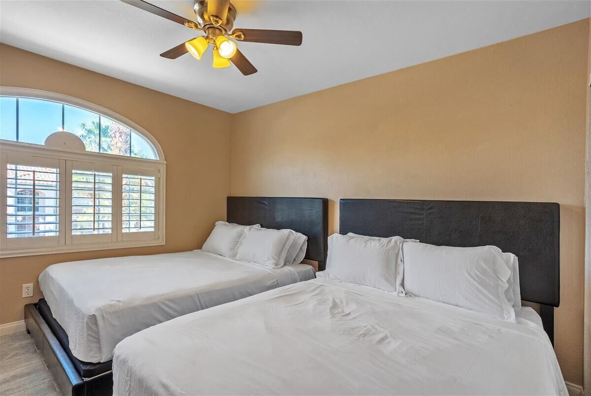 A bedroom with two beds, a ceiling fan, and a large window.