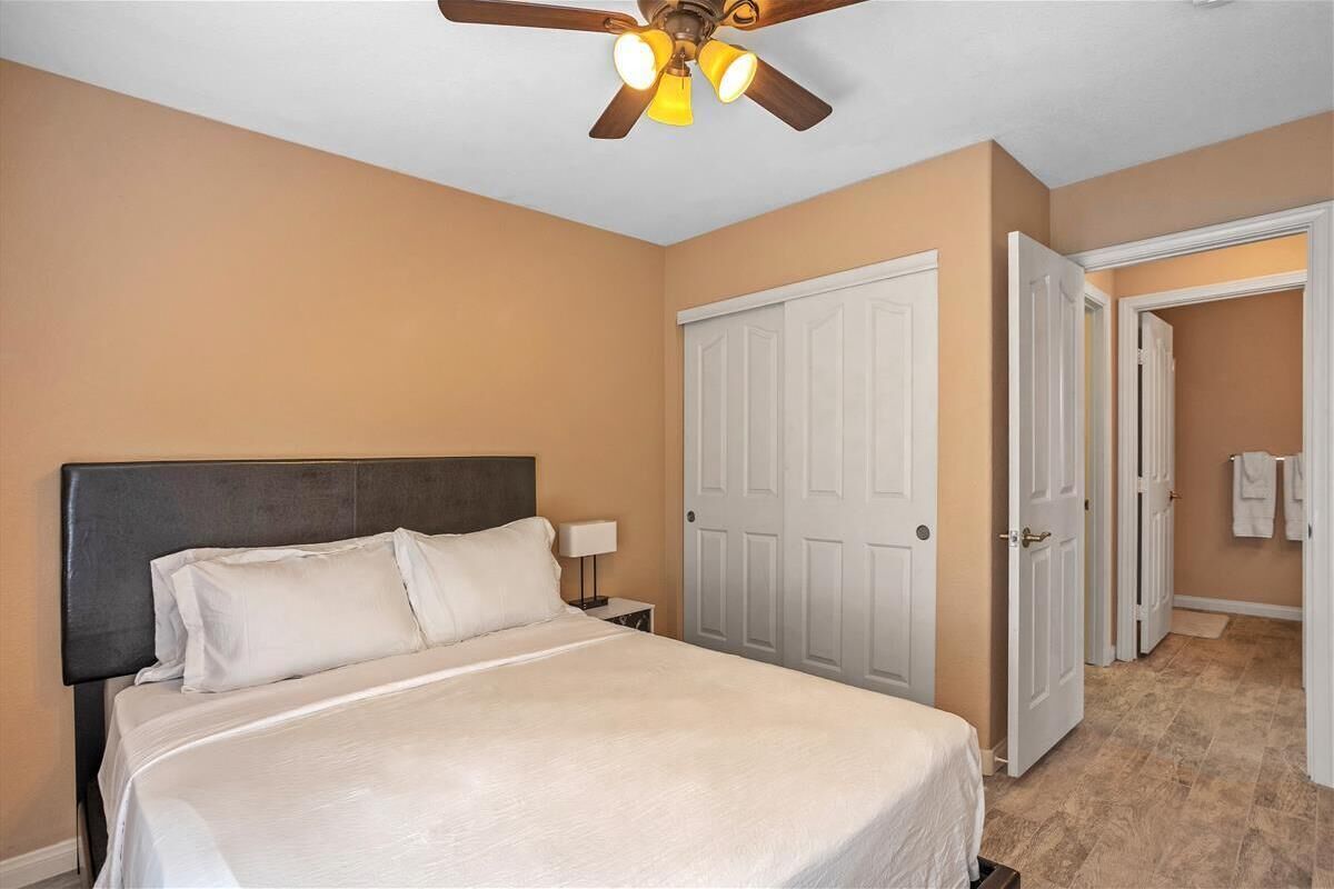 A hotel room with a bed, a ceiling fan, a white door, and a bathroom visible through an open door.